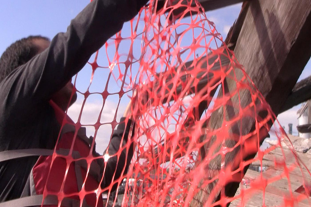 Close up of a person placing orange fencing on the sunken dock at the Gowanus canal in Brooklyn